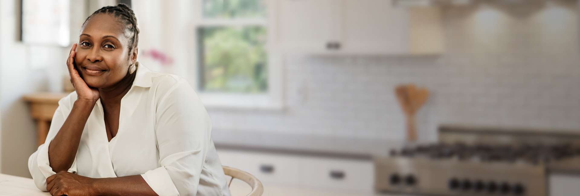 African American woman wearing a white button up shirt sitting at the kitchen table.